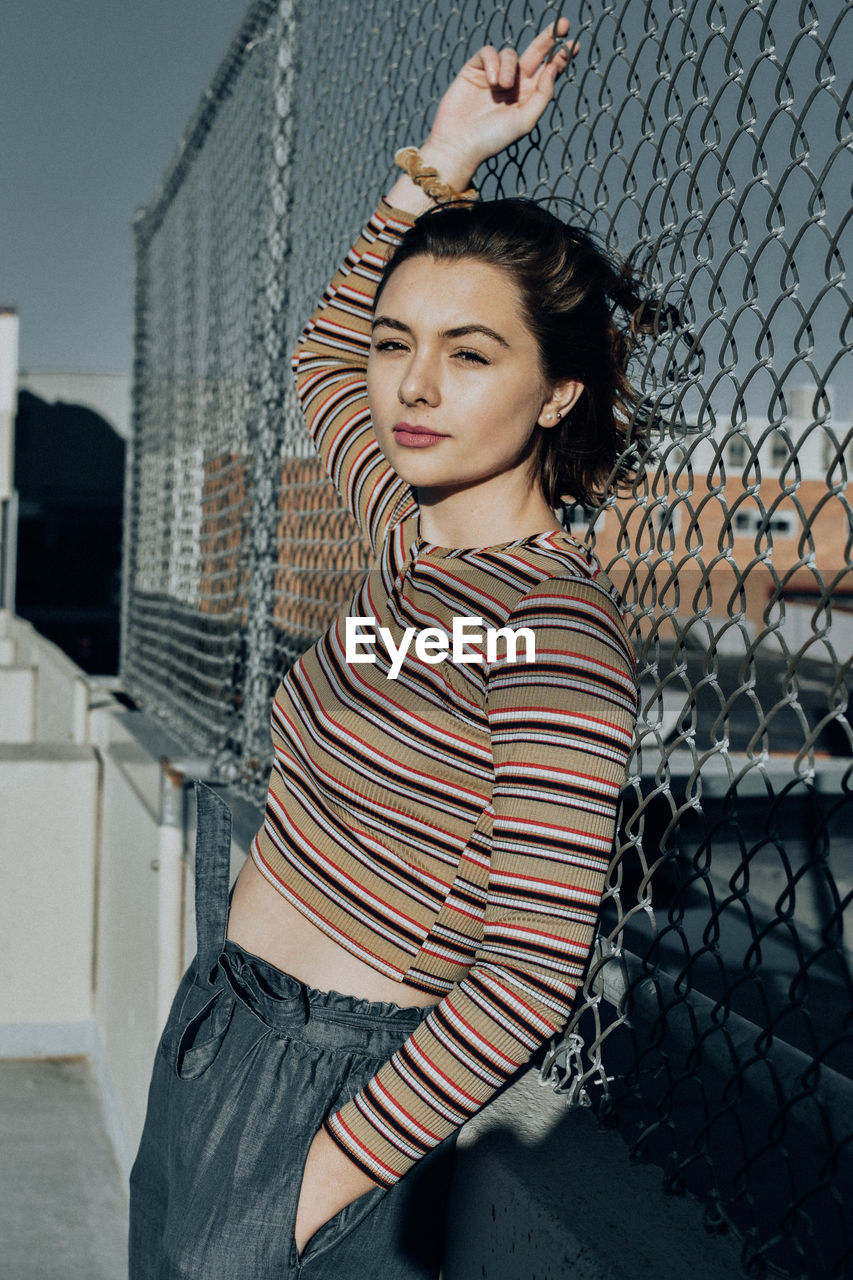 Portrait of young woman standing against fence