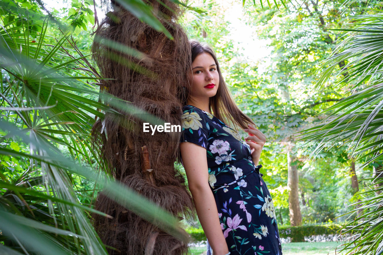 Portrait of smiling young woman by tree trunk