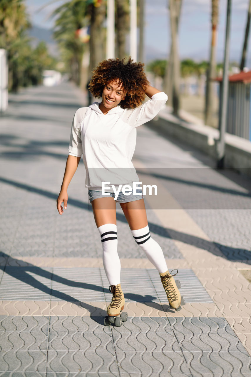 Full length portrait of young woman roller skating on footpath