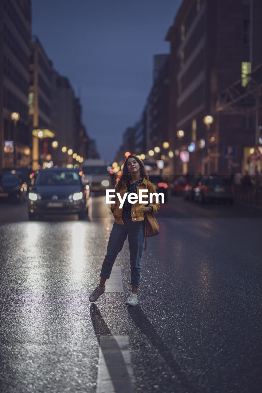 Portrait of young woman standing on road in city at night