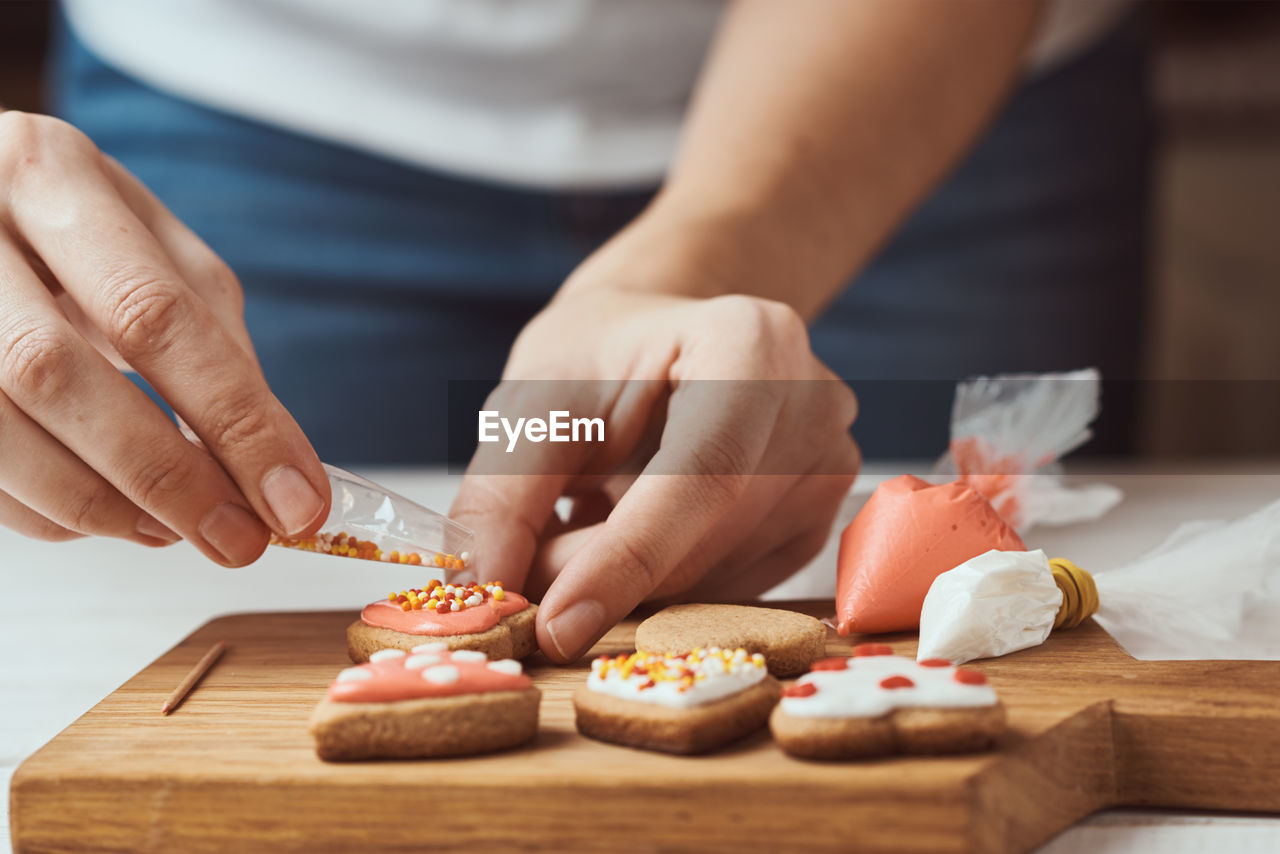 Decorating gingerbread cookies with icing. woman hands decorate cookies in shape of heart, closeup