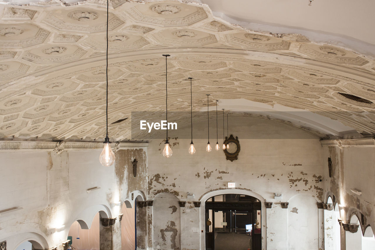 LOW ANGLE VIEW OF ILLUMINATED CHANDELIER HANGING FROM CEILING IN BUILDING