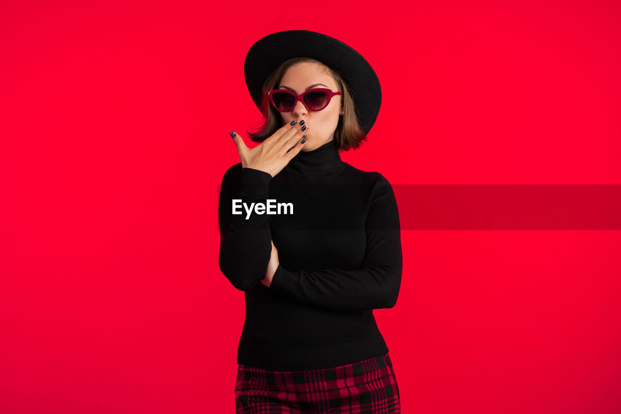 Portrait of smiling woman in sunglasses standing against red background