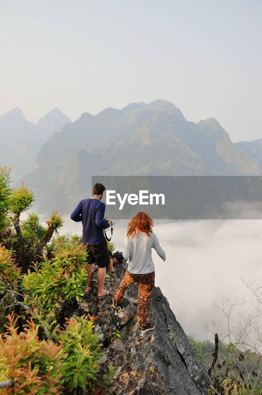 Rear view of couple standing on mountain against clear sky