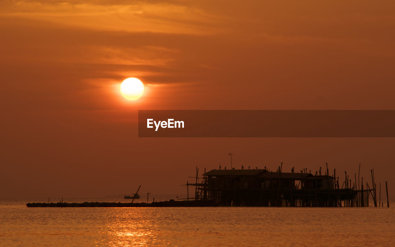 Silhouette built structure in sea against sky during sunset