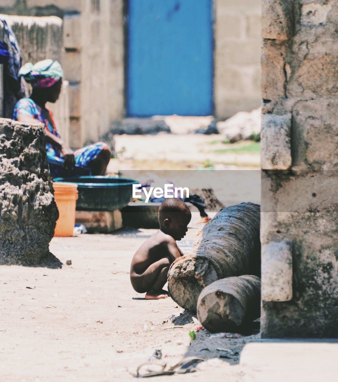 Naked boy crouching on alley with woman washing clothes