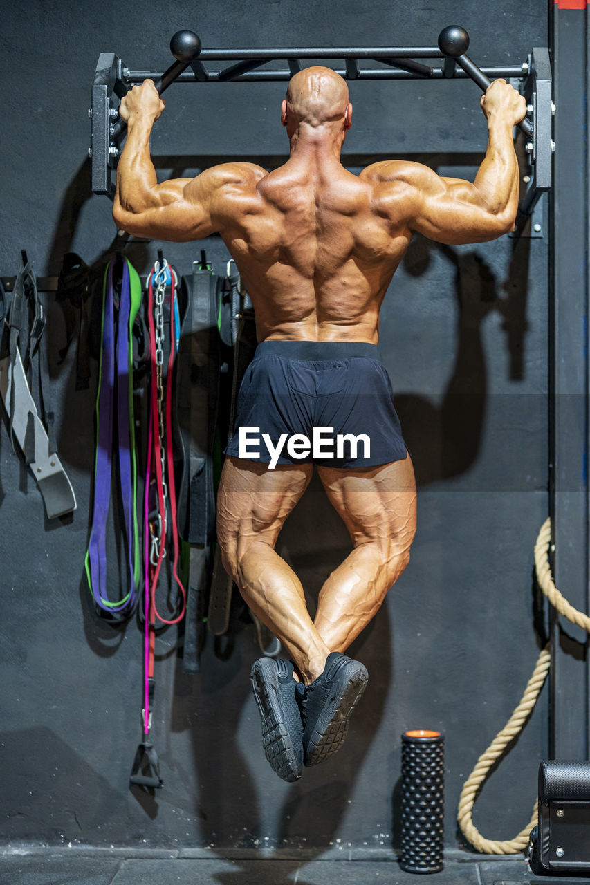 Shirtless bodybuilder practicing chin-ups in gym