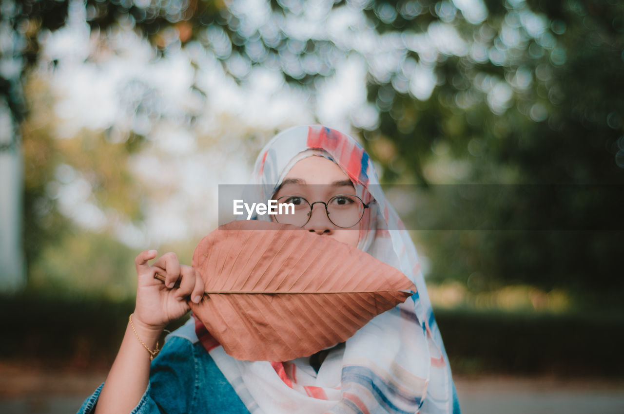 Portrait of teenage girl covering mouth with dry leaf 