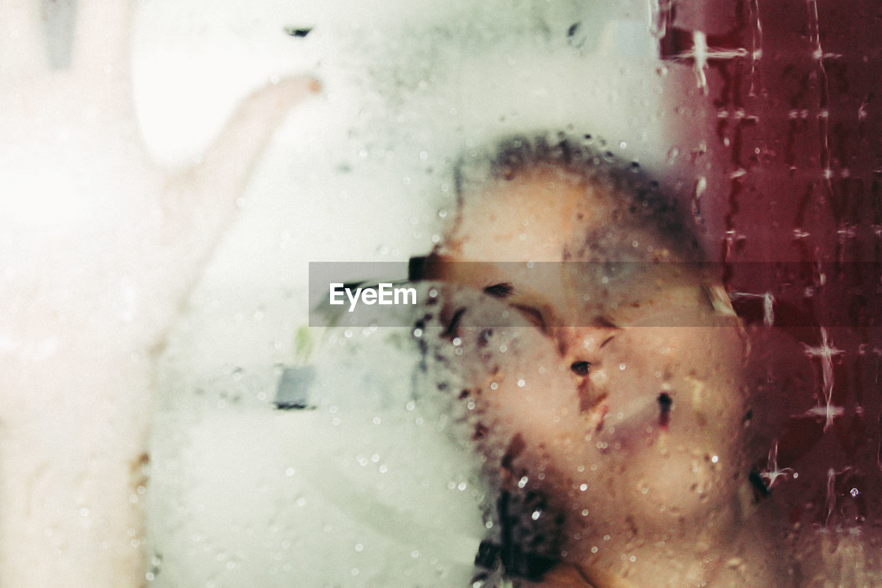 Close-up of young woman in bathroom seen through wet window