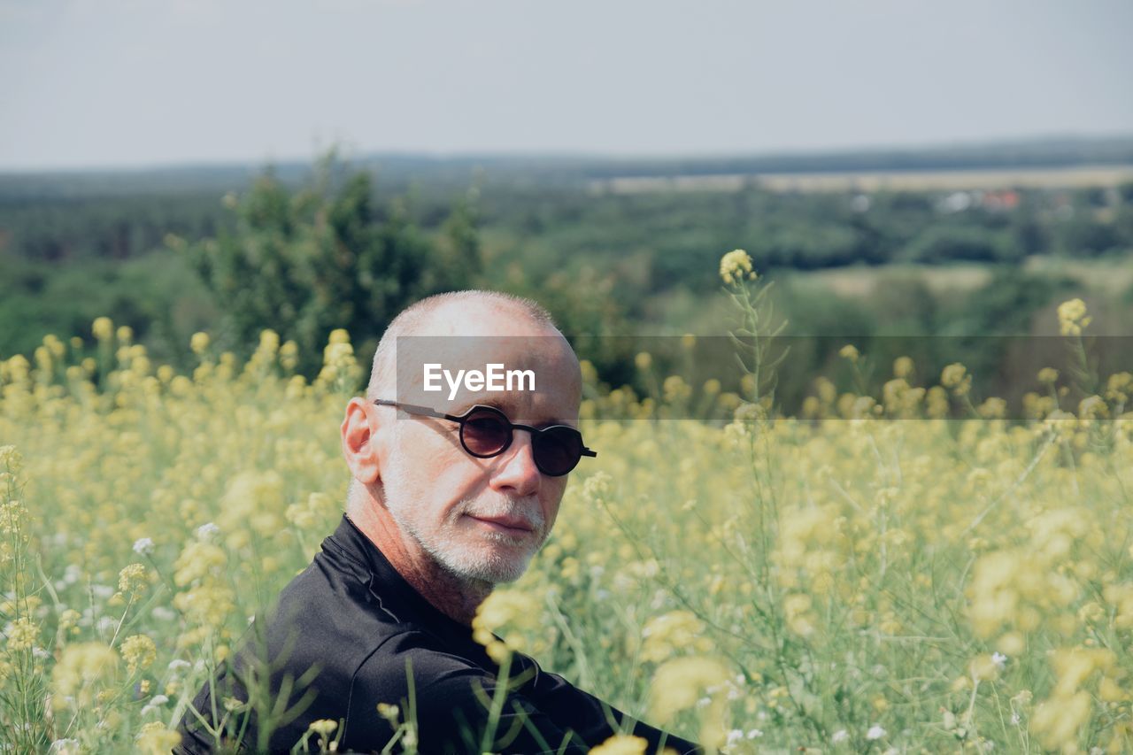 Portrait of man wearing sunglasses sitting amidst plants on land