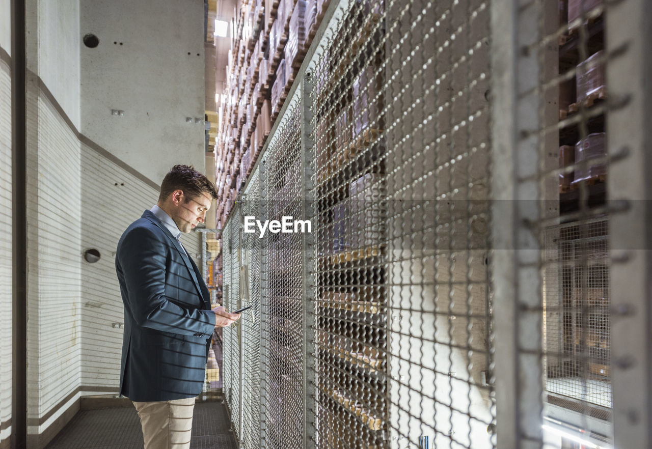 Man in automatized high rack warehouse looking at cell phone