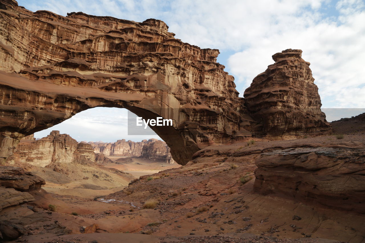 rock, arch, rock formation, sky, travel destinations, nature, scenics - nature, geology, landscape, environment, land, beauty in nature, travel, cloud, natural arch, non-urban scene, ancient history, valley, desert, no people, eroded, wadi, architecture, physical geography, formation, tranquility, climate, sandstone, mountain, outdoors, terrain, tourism, day, arid climate, extreme terrain, canyon, tranquil scene, dry, accidents and disasters, history, semi-arid, idyllic