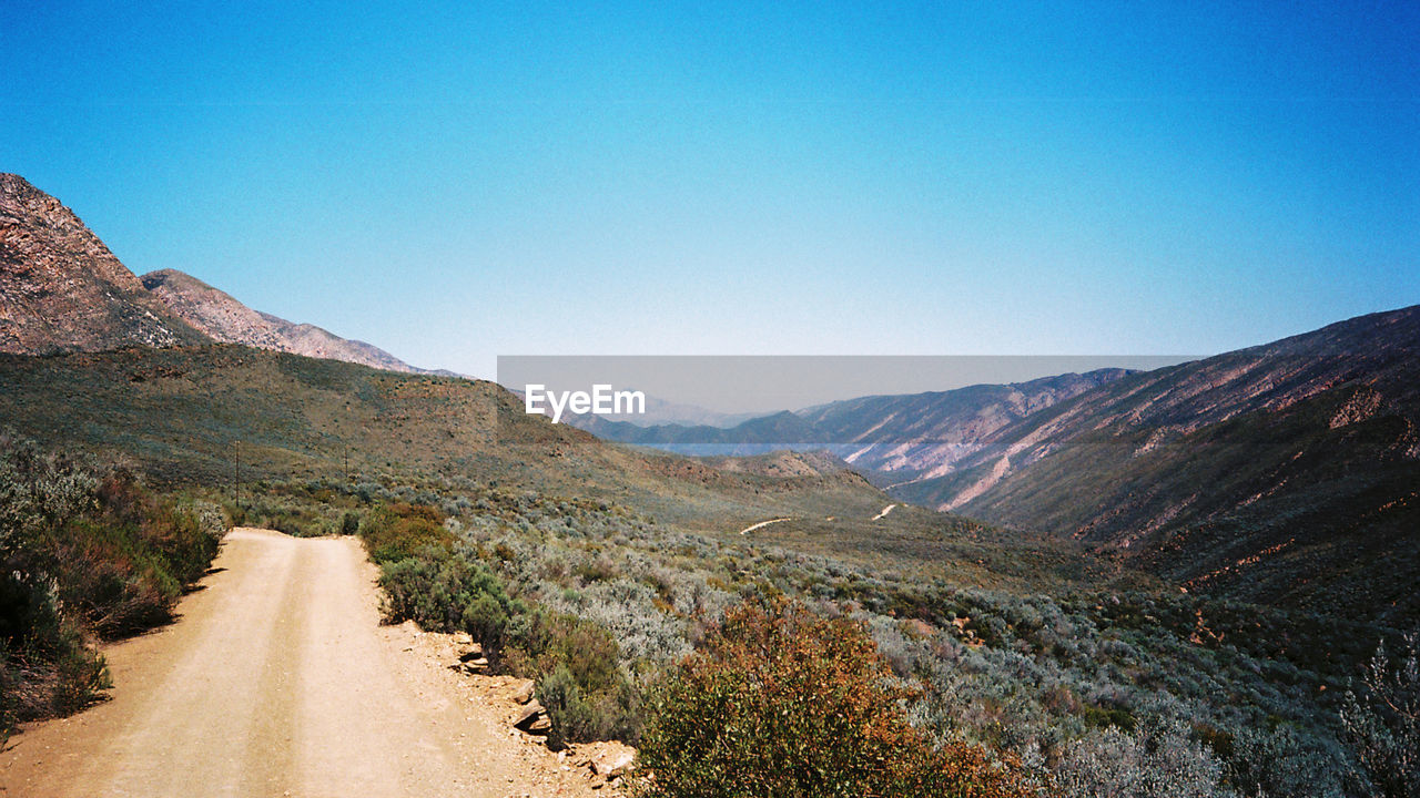 Dirt road by mountain against clear sky