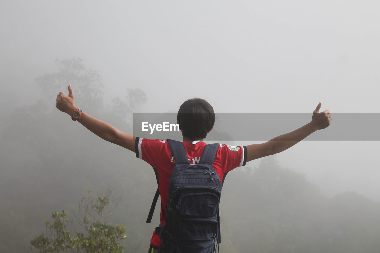 Rear view of man with arms outstretched standing in foggy weather