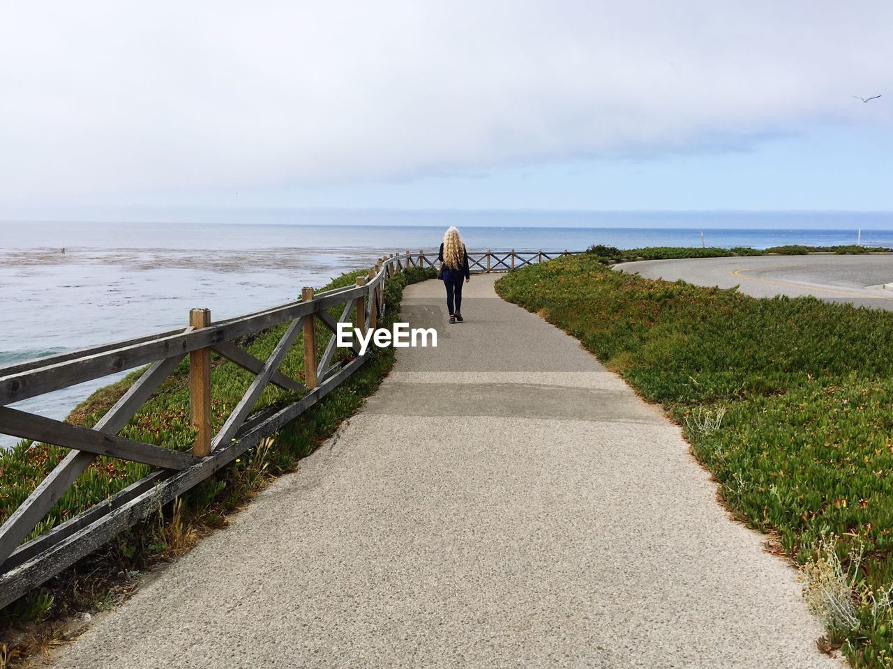 Rear view of woman walking on promenade by sea against sky