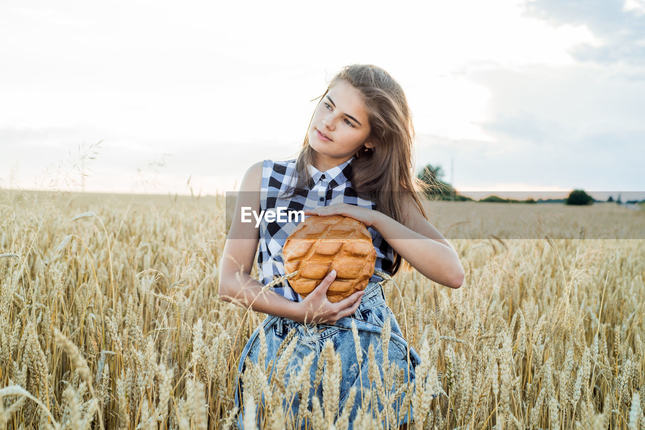 Teenager girl holding loaf of bread while standing amidst farm