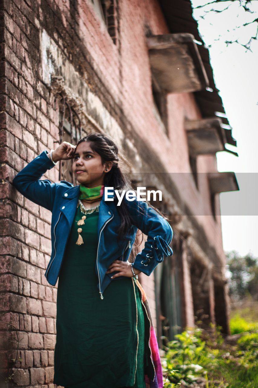 YOUNG WOMAN STANDING AGAINST BRICK WALL