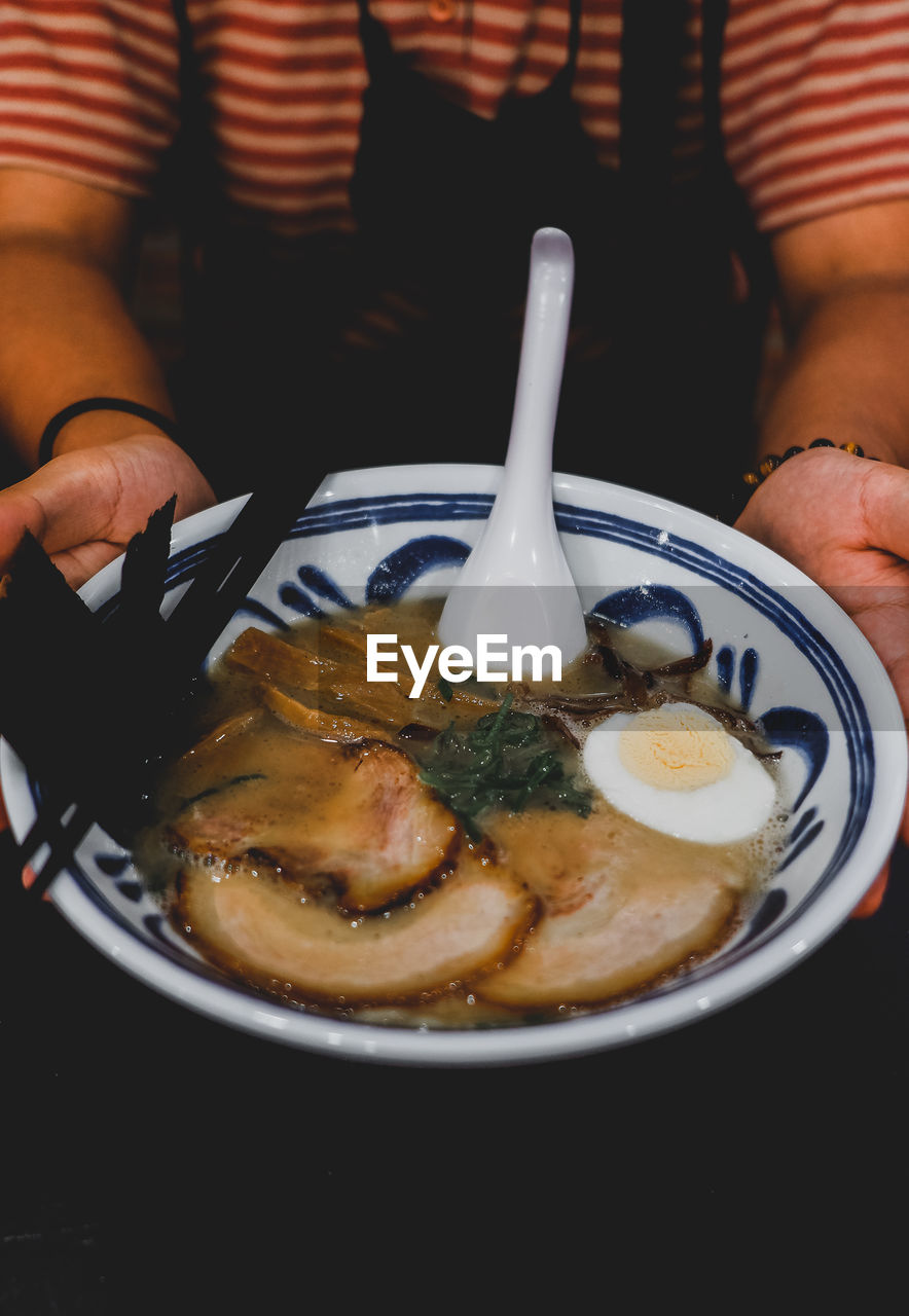 Close-up of hand holding tonkatsu ramen served in plate