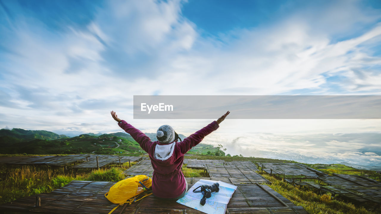 rear view of woman with arms raised standing on rock against sky