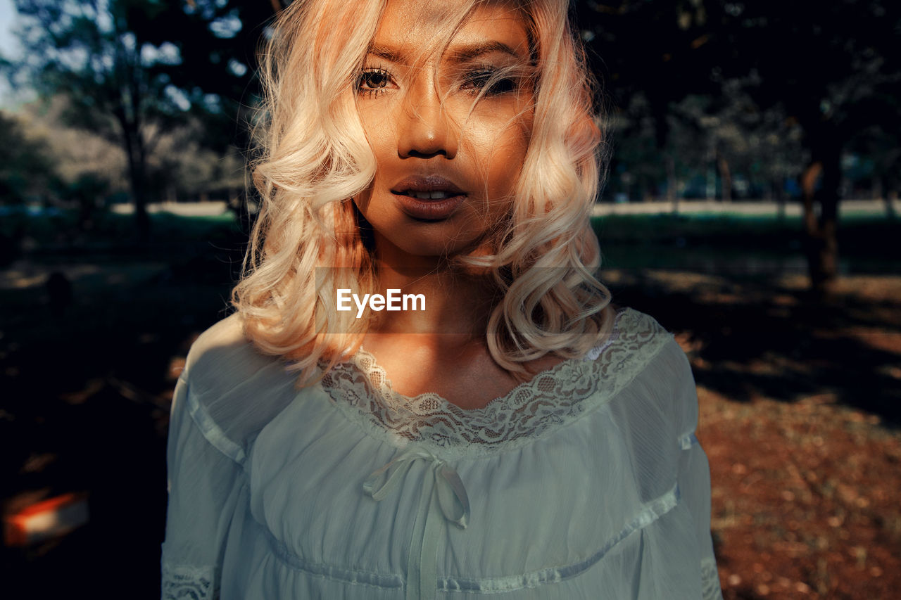 Close-up portrait of young woman standing against trees at park