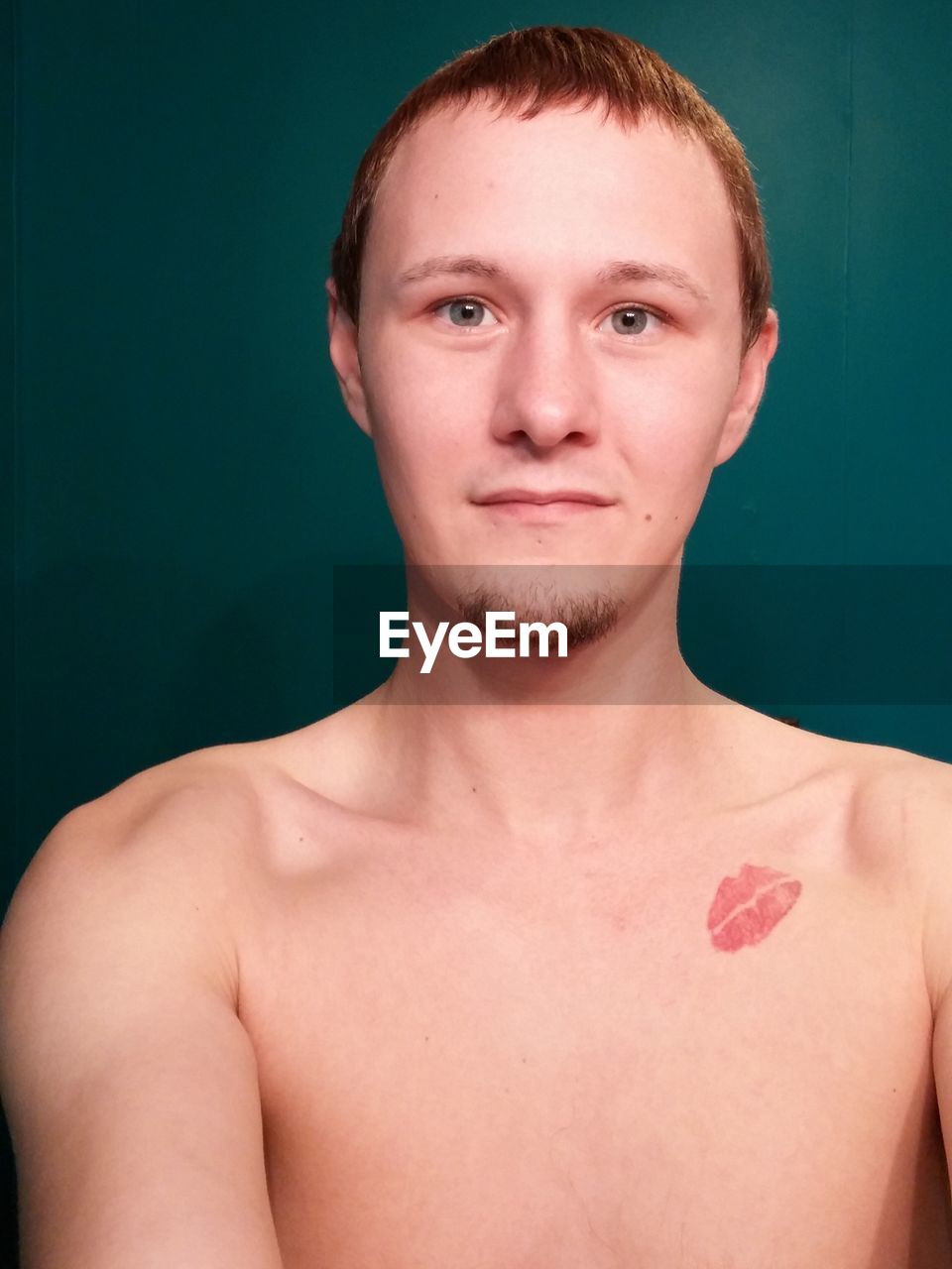 Portrait of handsome young man with lipstick kiss on chest against blue background