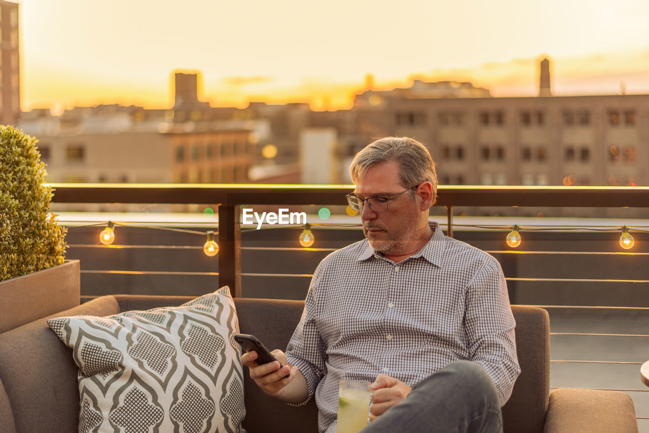 Mature man using phone at terrace during sunset