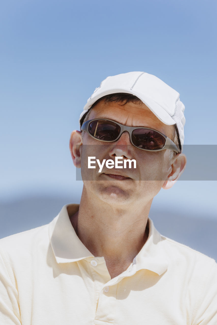 Man wearing sunglasses and cap against clear sky