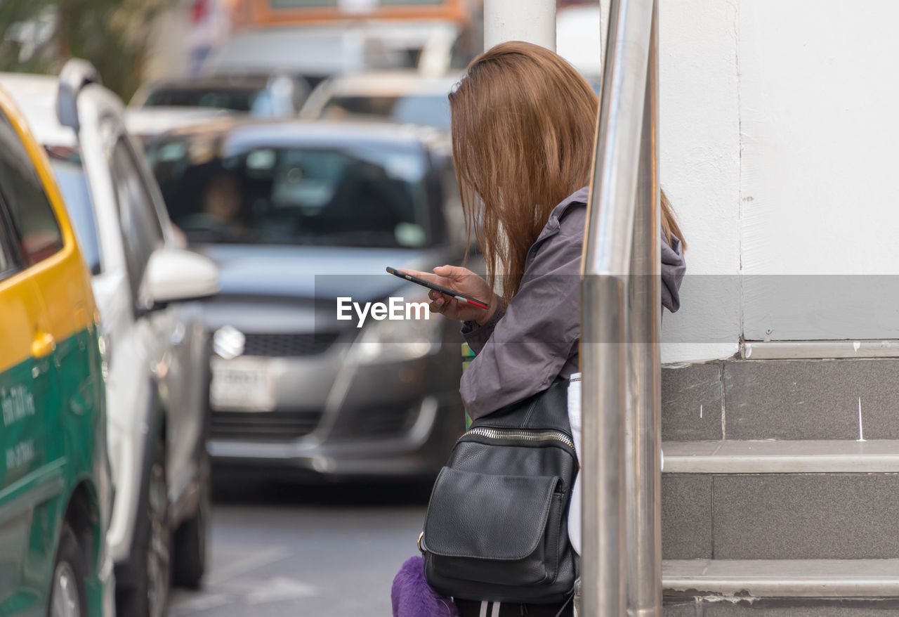 Side view of woman using phone while standing at bus stop