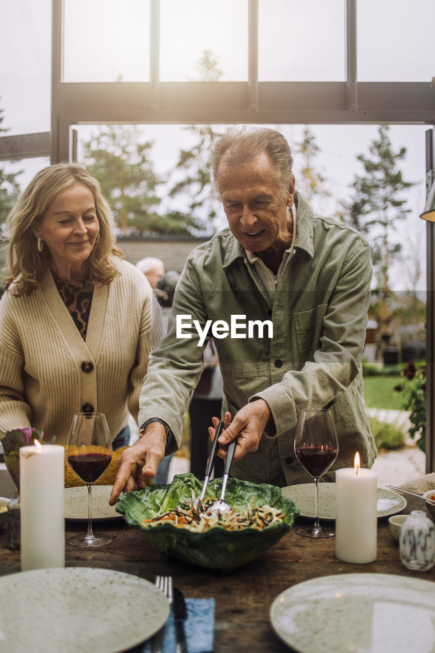 Senior man preparing dining table with female friend during party