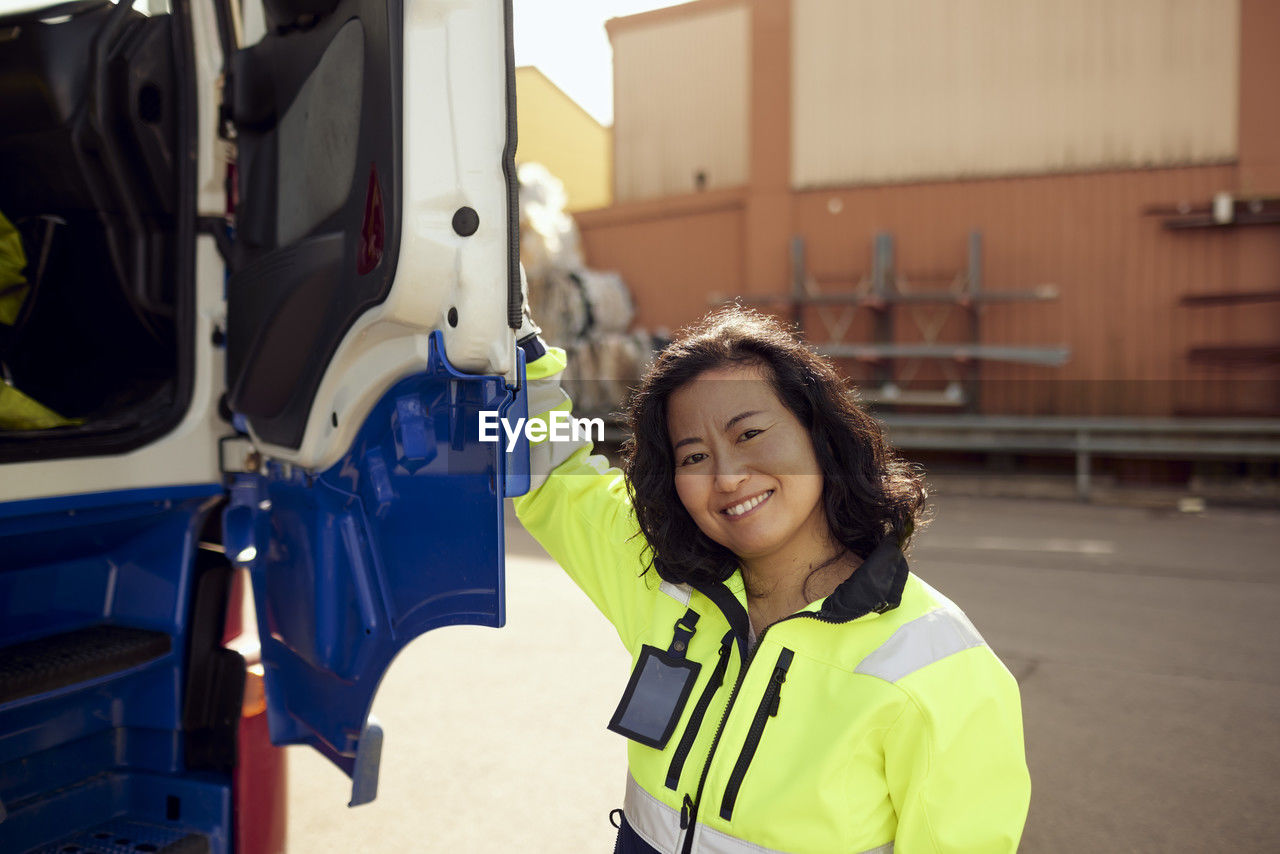 Portrait of smiling female worker opening door of truck outside industry