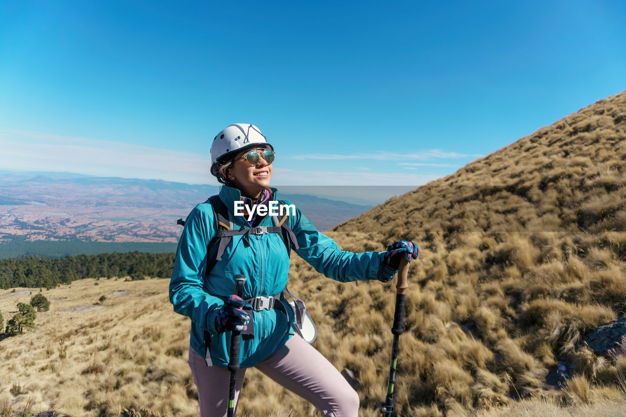 Smiling woman trekking against sky