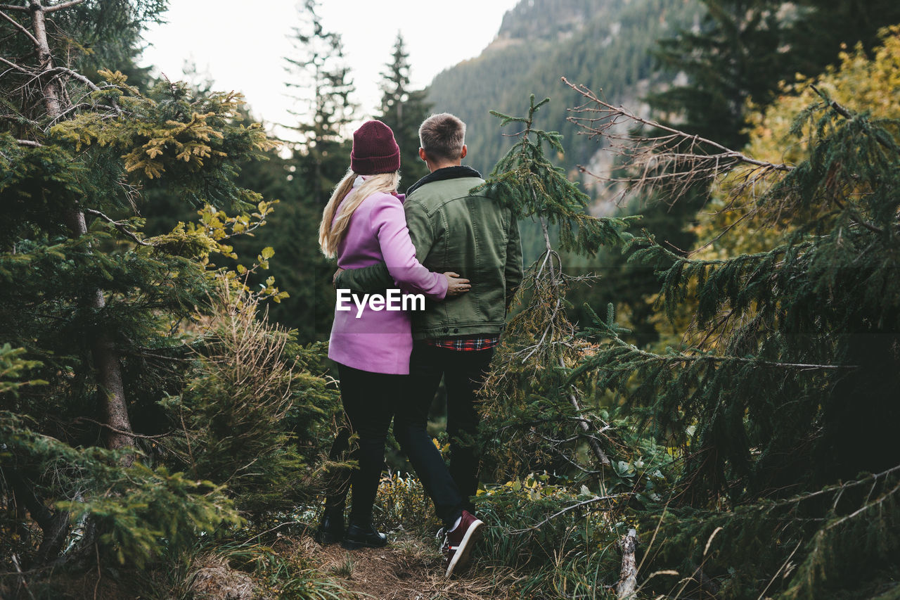 Rear view of couple standing amidst trees in forest