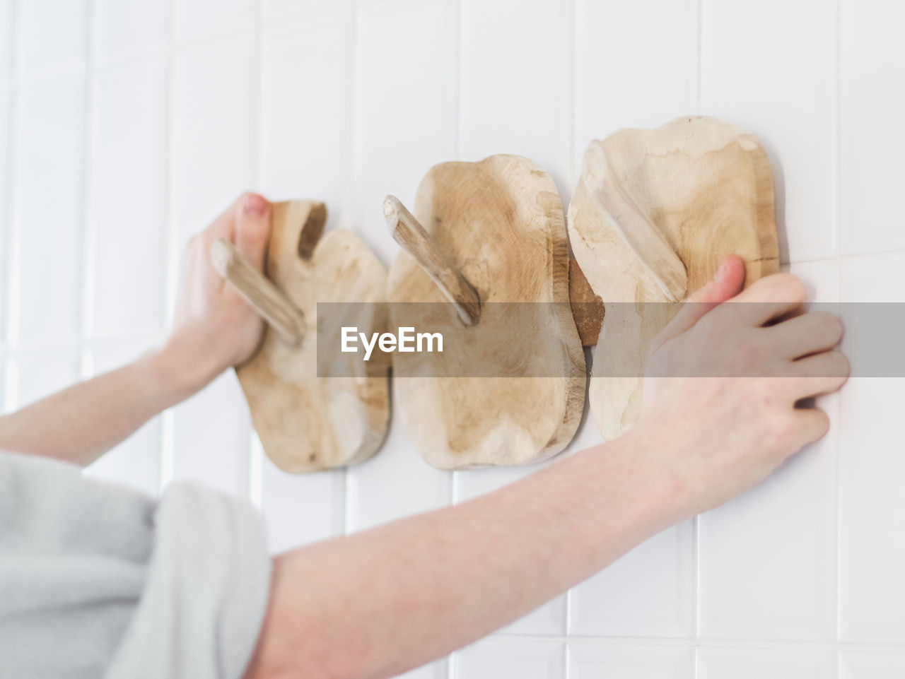 The hands of a young caucasian guy hangs a new wooden stylish and eco-friendly hanger on the wall