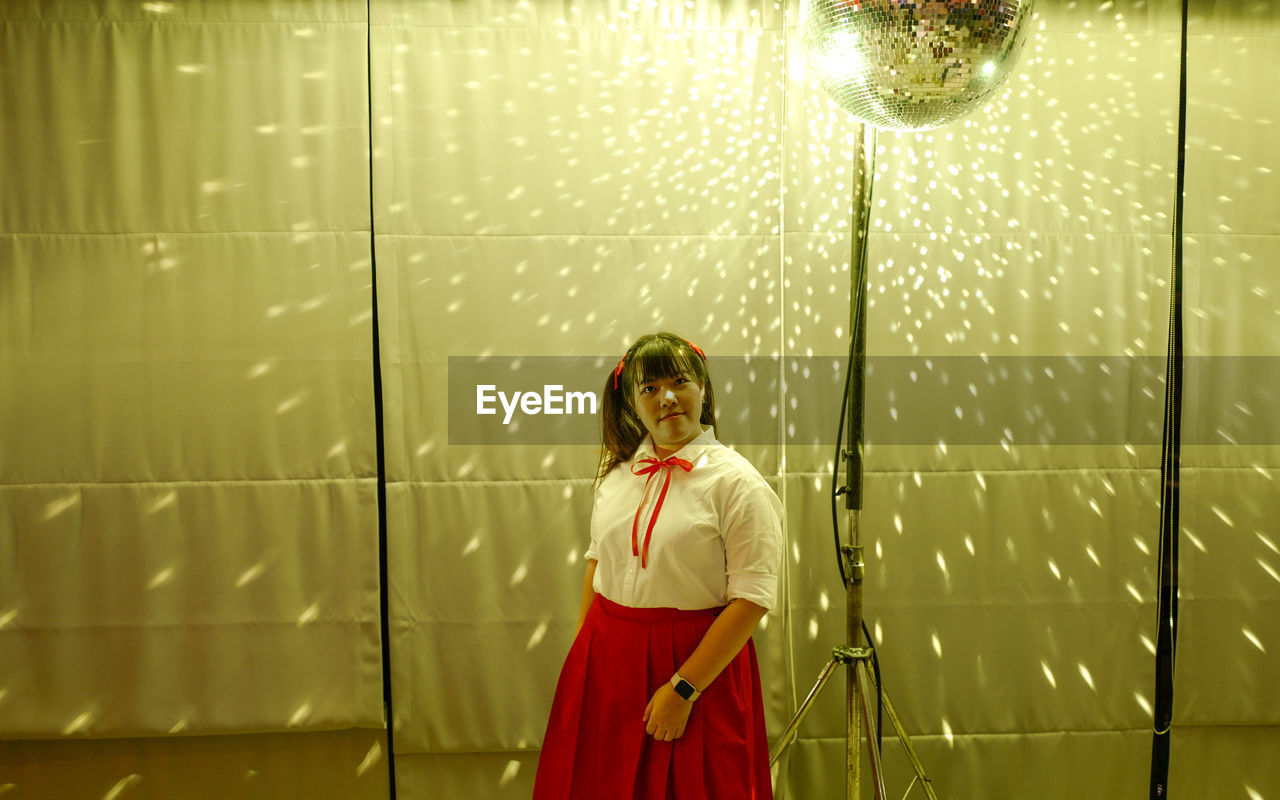 Portrait of woman standing against illuminated backdrop