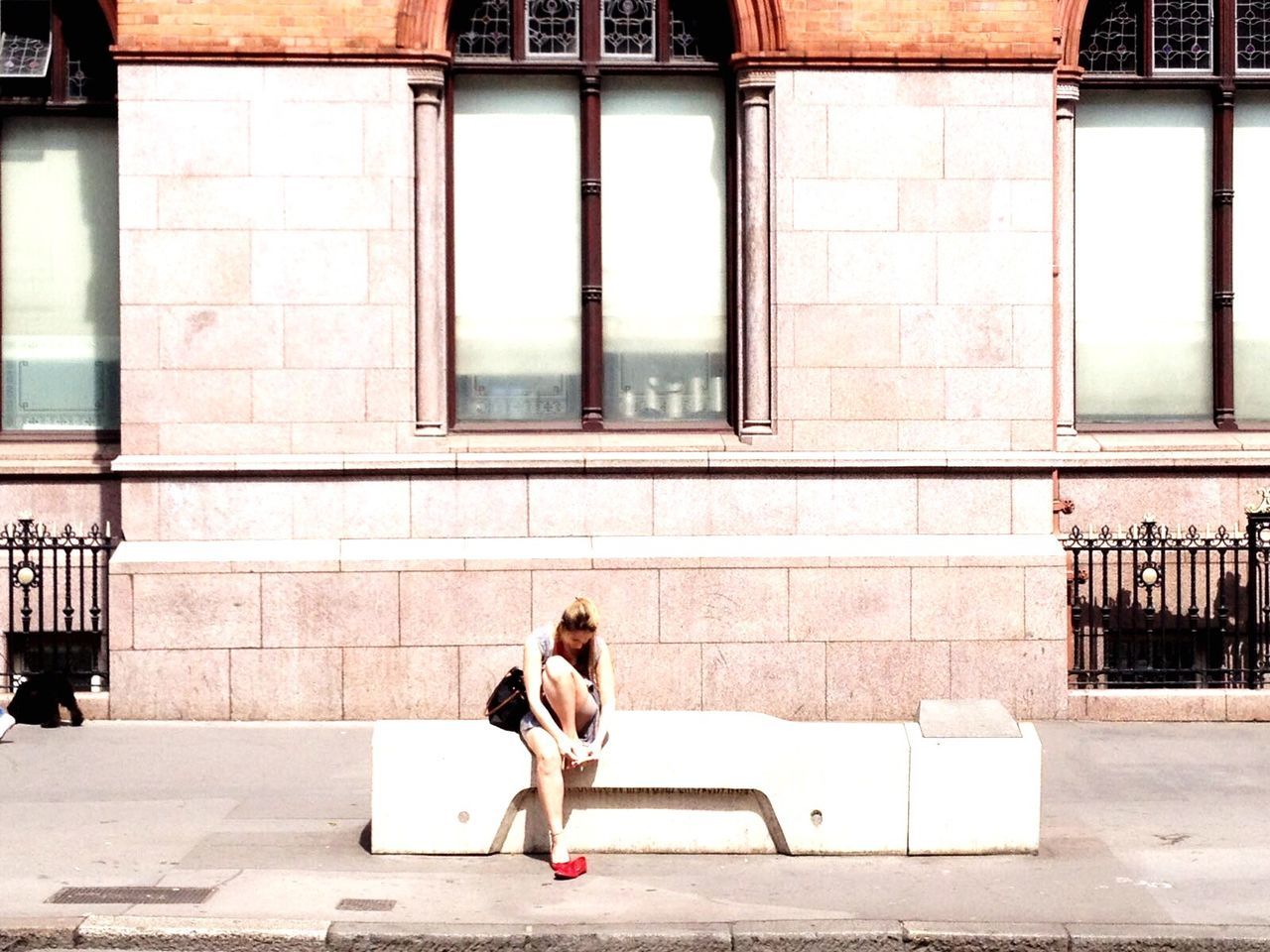 WOMAN SITTING ON SIDEWALK BY BUILDING