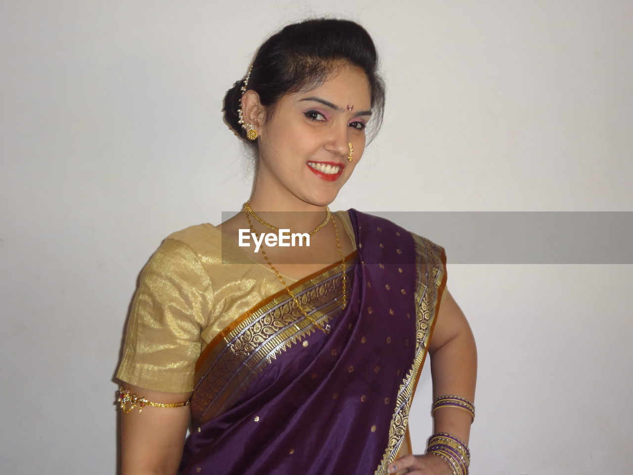 Portrait of smiling woman in sari standing against wall