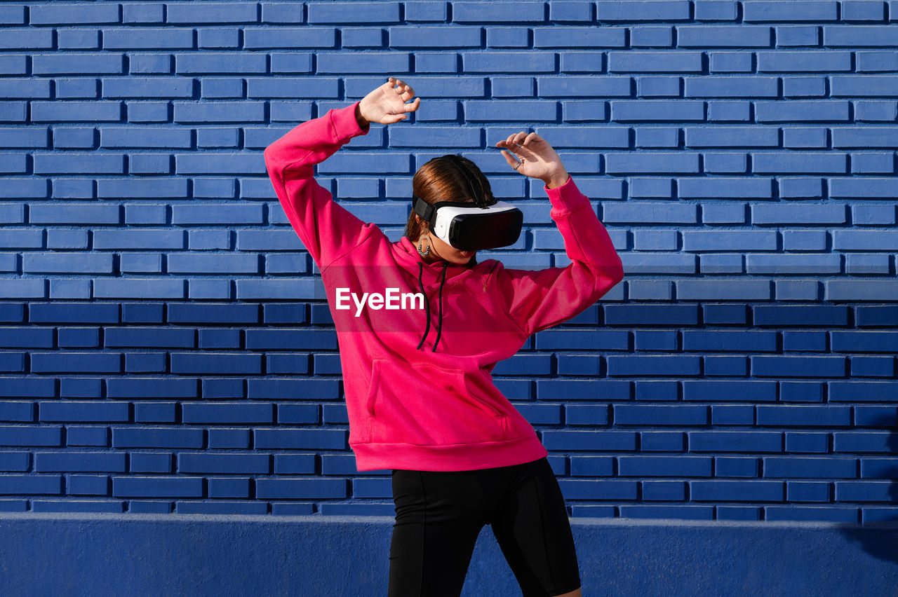 Caucasian woman using virtual reality glasses on the street on a background of blue bricks 