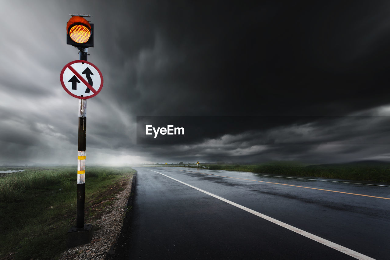 Road sign by wet road against sky