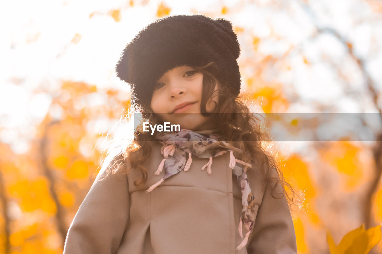 Close-up portrait of cute girl in warm clothing against tree