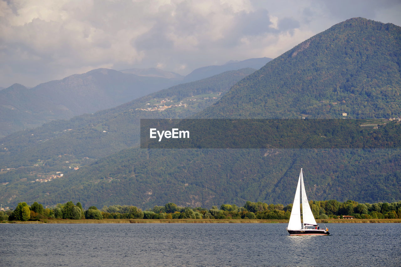 Sailboat sailing on sea by mountains against sky