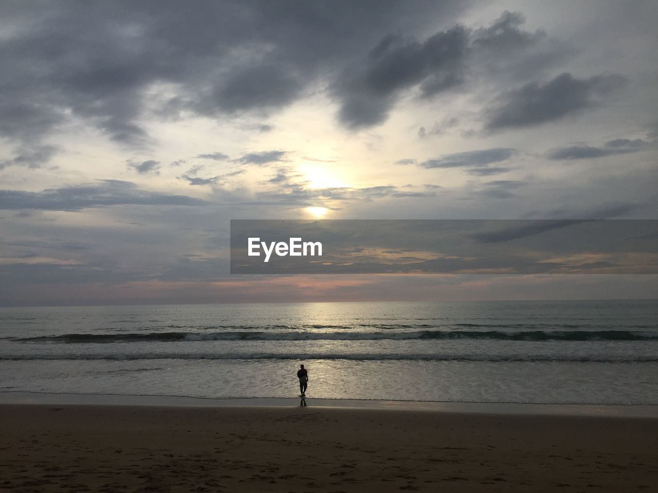 MAN STANDING ON BEACH AGAINST SKY DURING SUNSET