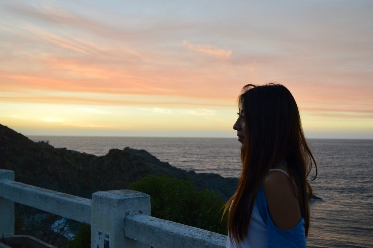 Young woman with long hair standing at beach against sky during sunset