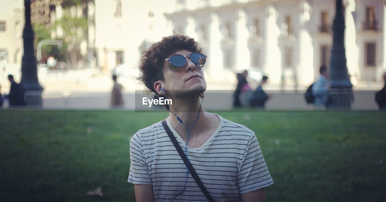 Close-up of young man wearing sunglasses and headphones while standing outdoors