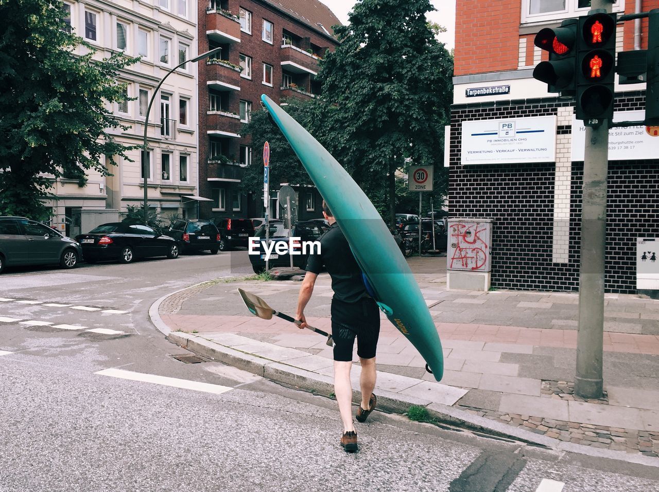 Rear view of man carrying canoe and oar on street in city