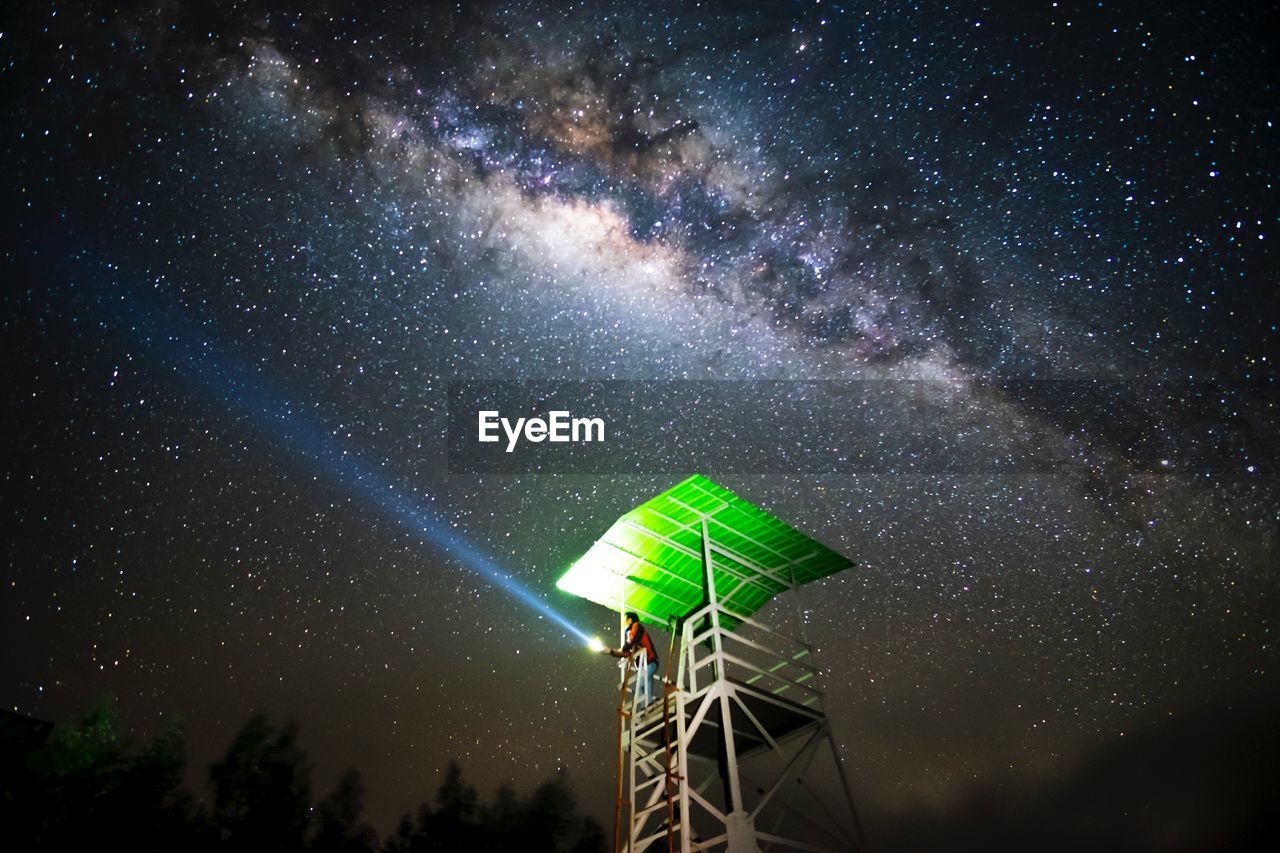 Low angle view of man holding flashlight while standing at observation point against sky during night