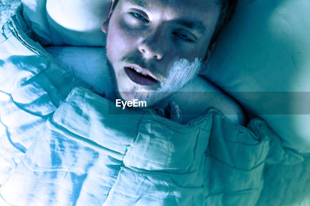 Sick man with cream on face lying down in bed