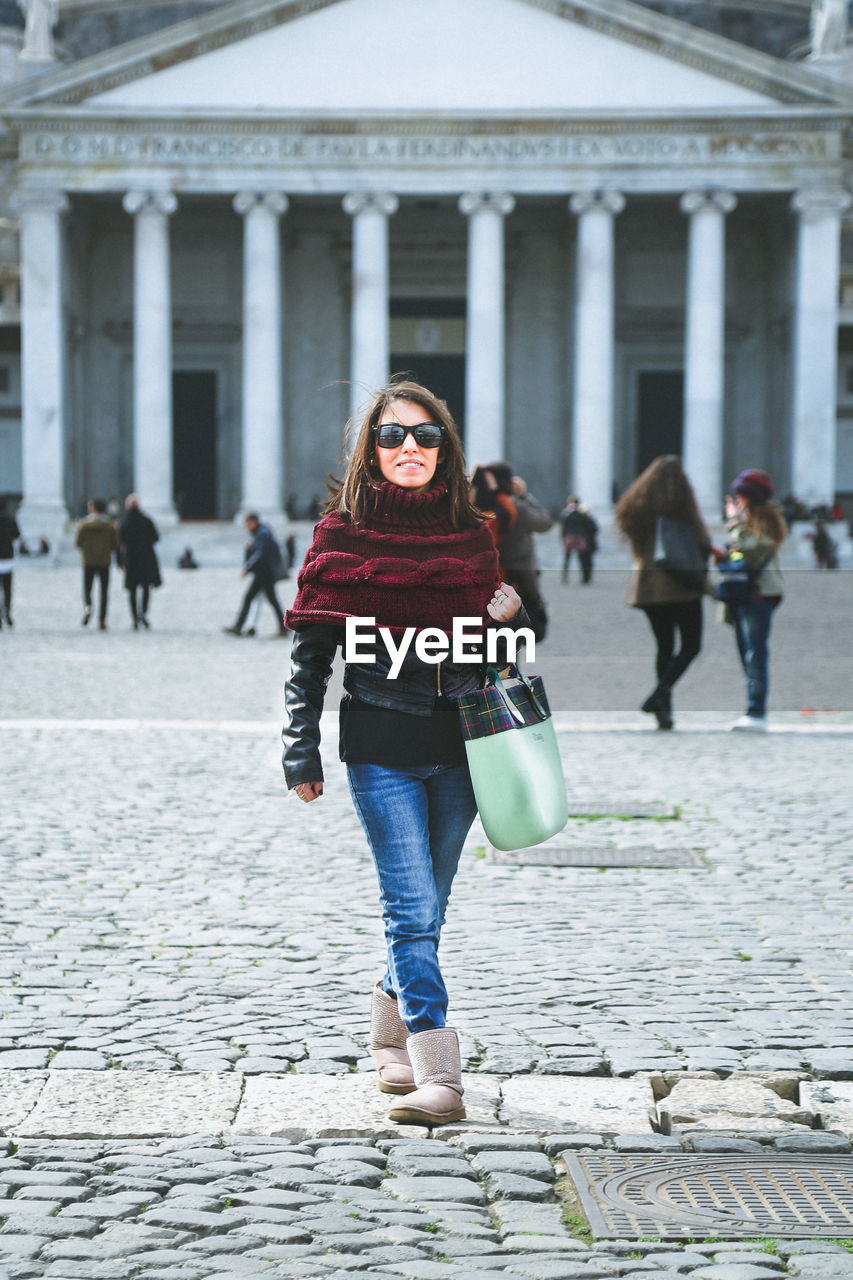 Full length portrait of woman walking against building in city