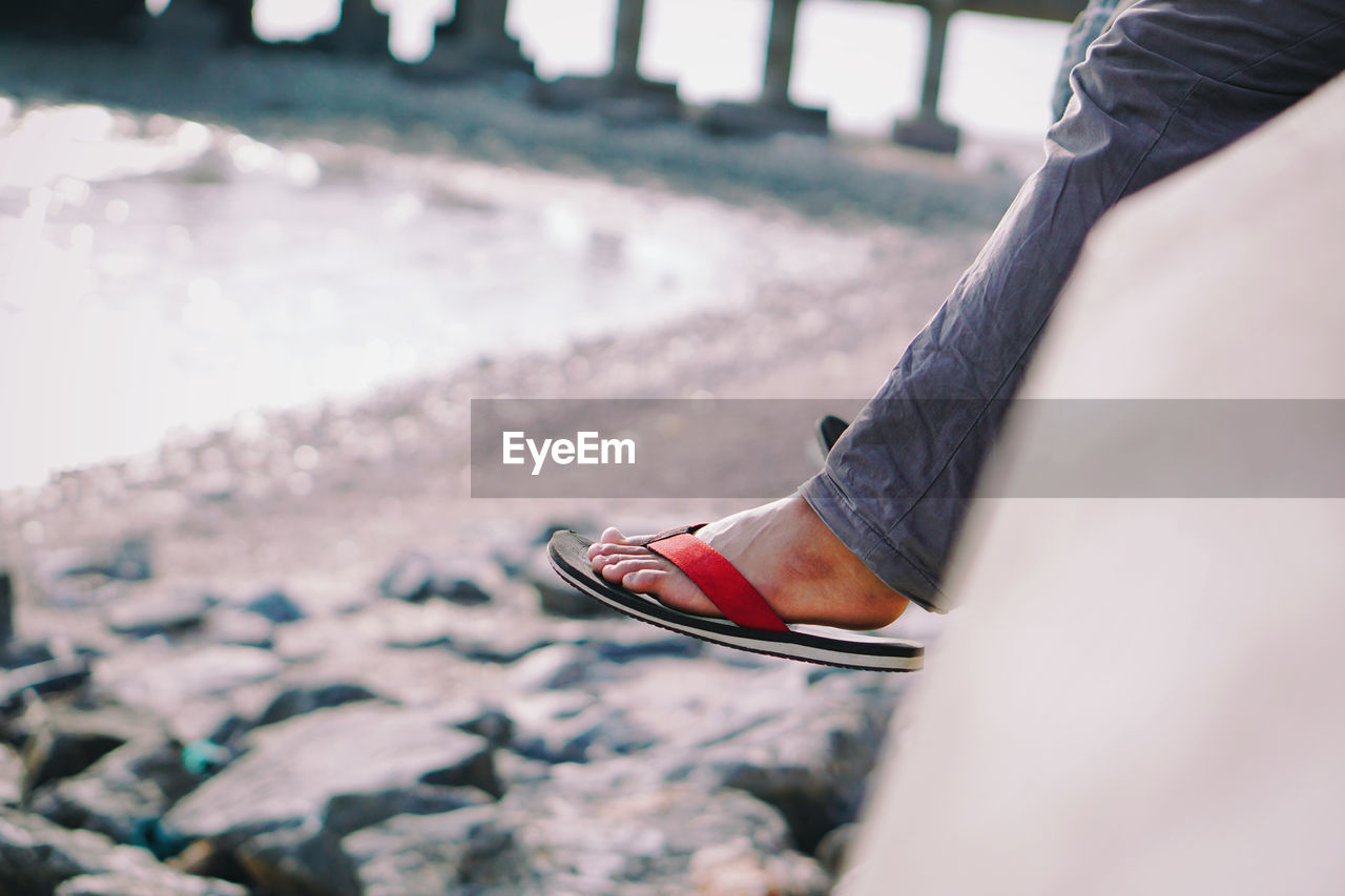 Low section of person with slipper sitting by sea