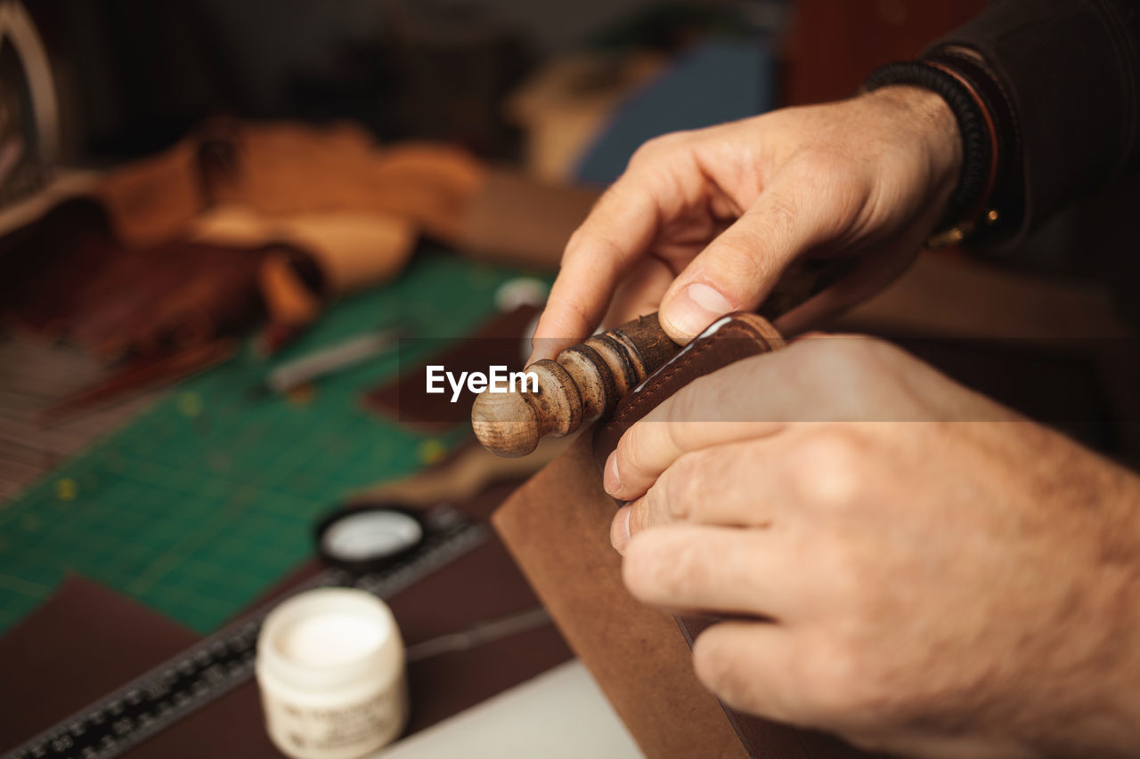 Wooden tool. tanner makes leather wallet, professional craftsman, closeup, indoors, authentic, 