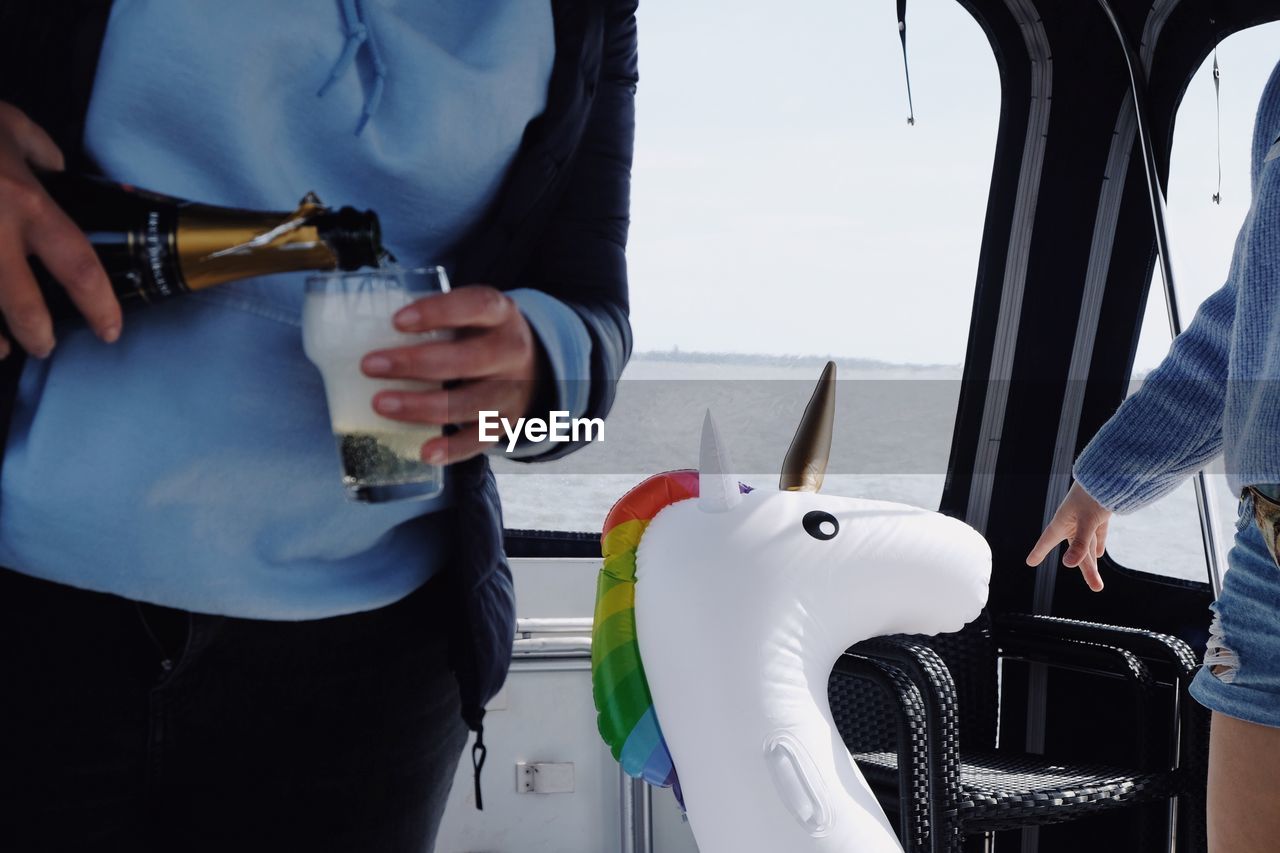 Midsection of woman pouring champagne in glass while standing with friend in yacht